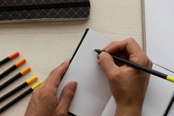 istock desk with a person's hands writing with a pen on the sheets of a notebook and colored pencils in the background on a desk, office instruments 1337960875