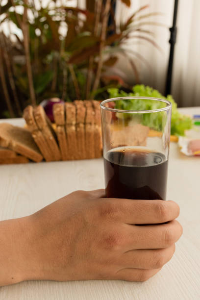hand holding a glass with a drink in the background fresh vegetables next to a mold of sliced wholemeal bread, drinks and food at home, snack ingredients - carbohydrate freshness food and drink studio shot imagens e fotografias de stock