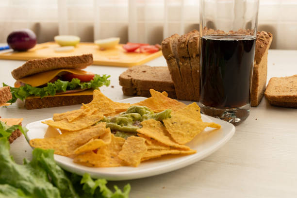 plate of crunchy nachos accompanied by guacamoles, sandwich with cheese, lettuce and tomato, a mold of sliced whole wheat bread and a glass with drink, food and drink as a snack - carbohydrate freshness food and drink studio shot imagens e fotografias de stock