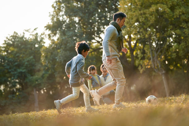 padre asiático jugando al fútbol con su hijo mientras madre e hija miran - park child asia lifestyles fotografías e imágenes de stock