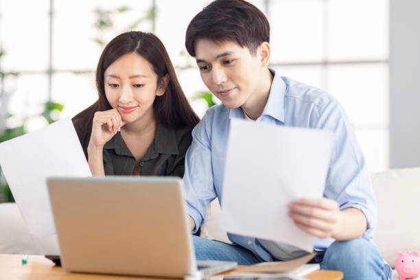 istock Young husband and wife holding paperwork and using laptop at home. 1337974870