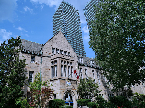 Toronto, Canada - August 31, 2021:  Old gothic style stone building at the University of Toronto's downtown campus, surrounded by high rise buildings.