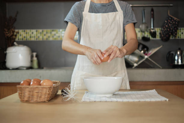 istock Female cook in a white apron is cracking an egg in home's kitchen. 1337987081