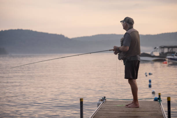 Senior Man Fly-Fishing at Sunset Senior Man Fly-Fishing at Sunset at the lake. He is standing on a pier at Lac St-Joseph, Quebec, Canada. bass fish photos stock pictures, royalty-free photos & images