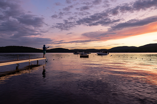 Man Fly-Fishing at Sunset at the lake. He is standing on a pier at Lac St-Joseph, Quebec, Canada.