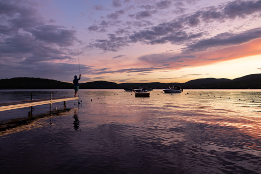 Man Fly-Fishing at Sunset at the lake. He is standing on a pier at Lac St-Joseph, Quebec, Canada.