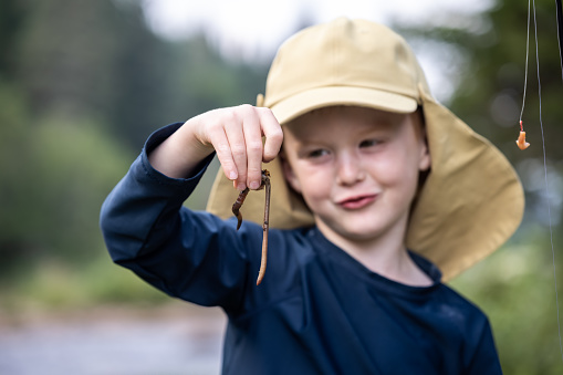 Cute Redhead Boy Showing an Earthworm and looking at camera and smiling. He is preparing his fishing bait to go fishing.