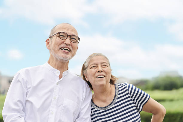 couple âgé debout avec un sourire contre le ciel bleu - senior adult outdoors wellbeing sky photos et images de collection