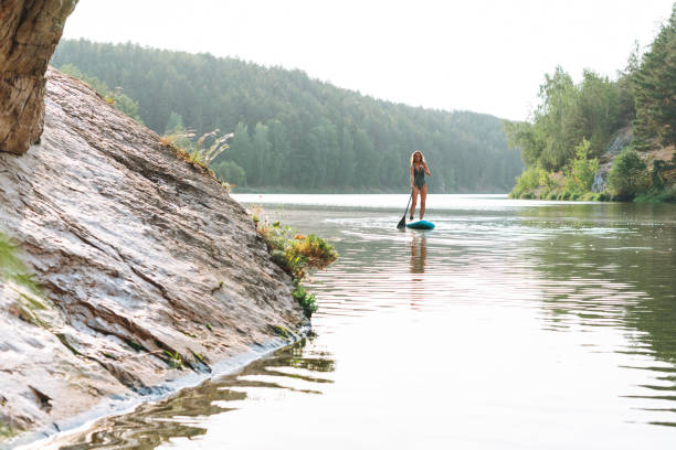 la jeune femme mince en sweemsuit vert sur un bateau de sup avec rame flottant sur la rivière, week-end et voyage local - bodysurfing photos et images de collection