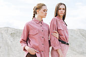 Fashion beauty portrait of young women sisters in pink organic velvet shirts on desert background
