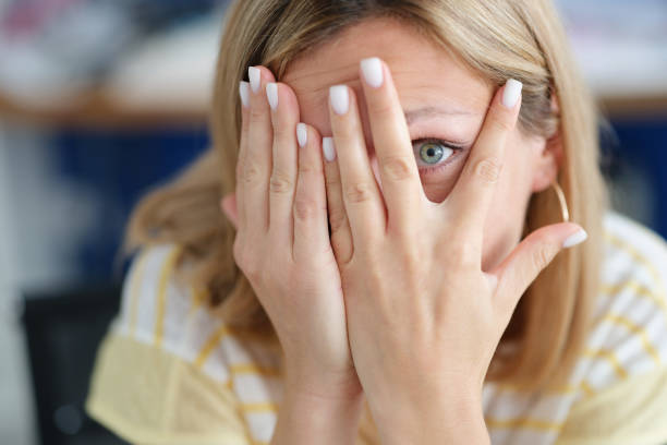 Woman covers face with hand looking through fingers. Facial expressions of emotion and suffering.