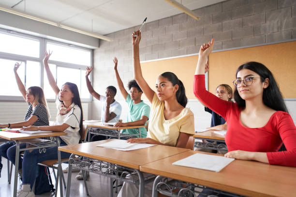istock Multi-ethnic students in class with hands raised. Concentrated young people with serious faces answering the teacher's question. 1338006326