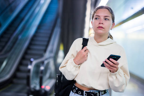 istock Young positive lady with smartphone standing on the escalator 1338007527