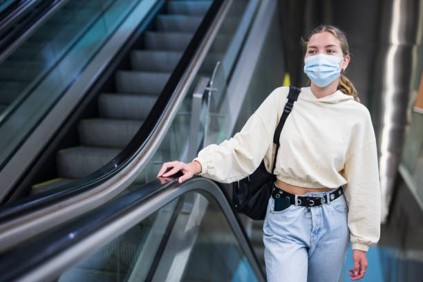 istock Young girl in protective face mask, standing on the escalator 1338007528