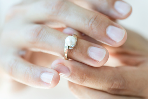 Hand of an unrecognizable female is about to wear a pearl ring.