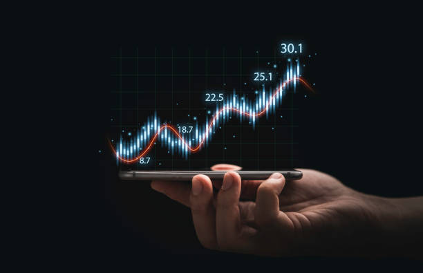 istock Trader hand holding smartphone with stock market graph chart on dark background for technical investment analysis concept. 1338008548