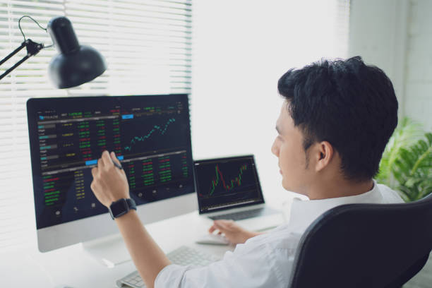istock Analyzing data. Back view of young businessman or trader pointing on the data on computer screen with pen while working his modern office. 1338016720