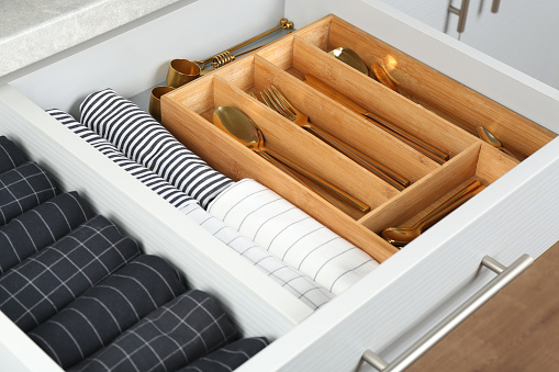 Open drawer with different utensils and folded towels. Order in kitchen