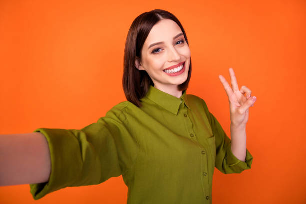 Photo of cool brunette hairdo millennial lady do selfie show v-sign wear green shirt isolated on orange color background stock photo