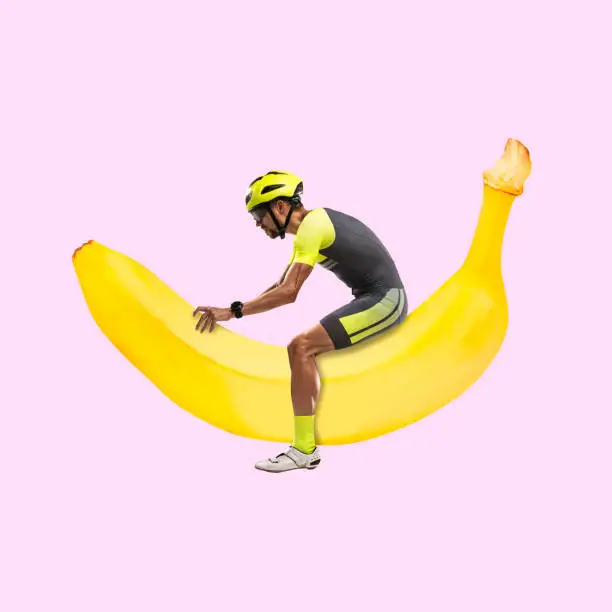 Contemporary art collage of young cyclist in helmet riding on banana instead bike isolated over pink background. Side view. Extraordinary image. Concept of healthy lifetyle, fit, sport, ad