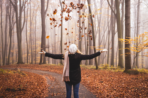 Happy woman throwing autumn leaves in the air. Enjoyment during hike in woodland at fall season
