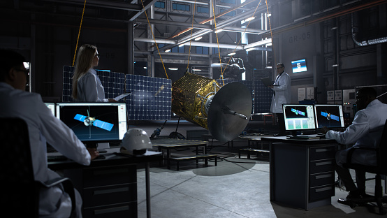Engineer and Technician Working on Satellite Construction. Aerospace Agency: Diverse Team of Scientists Using Technological Equipment and Laptop Computer to Develop Spacecraft for Space Exploration.