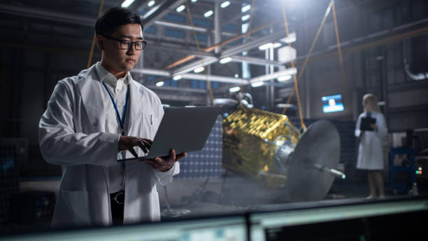 istock Industrial Engineer Working on Artificial Satellite Construction. Aerospace Agency: Asian Scientist Using Laptop Computer to Develop Spacecraft for Space Exploration and Data Communication. 1338031149