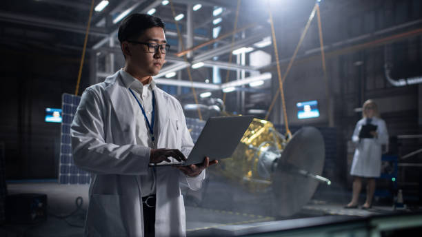 istock Industrial Engineer Working on Artificial Satellite Construction. Aerospace Agency: Asian Scientist Using Laptop Computer to Develop Spacecraft for Space Exploration and Data Communication. 1338031677