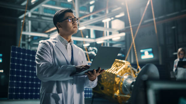 istock Industrial Engineer Working on Artificial Satellite Construction. Aerospace Agency: Asian Scientist Using Laptop Computer to Develop Spacecraft for Space Exploration and Data Communication. 1338031728