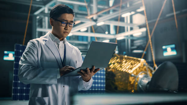 istock Industrial Engineer Working on Artificial Satellite Construction. Aerospace Agency: Asian Scientist Using Laptop Computer to Develop Spacecraft for Space Exploration and Data Communication. 1338031788