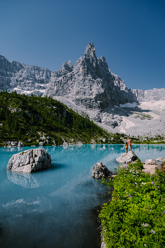 Morning with clear sky on Lago di Sorapis in the Italian Dolomites, milky blue lake Lago di Sorapis, Lake Sorapis, Dolomites, Italy. Couple man and woman mid age walking by the lake in the mountains