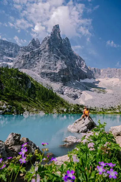 Morning with clear sky on Lago di Sorapis in the Italian Dolomites, milky blue lake Lago di Sorapis, Lake Sorapis, Dolomites, Italy. Couple man and woman mid age walking by the lake in the mountains