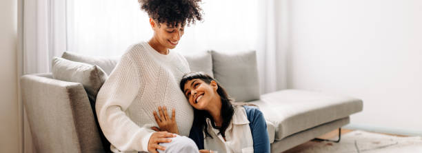 lesbian mother-to-be listening to her unborn baby kicking - homosexual family lesbian parent imagens e fotografias de stock