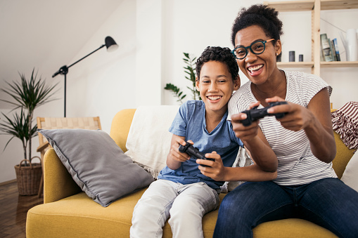 African American woman and her son playing video games at home and having fun.