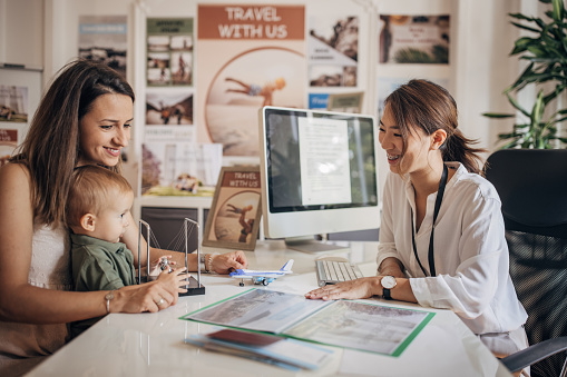 Group of people, single mother with baby son in modern travel agency talking to a woman who is working there, they are planning a vacation.