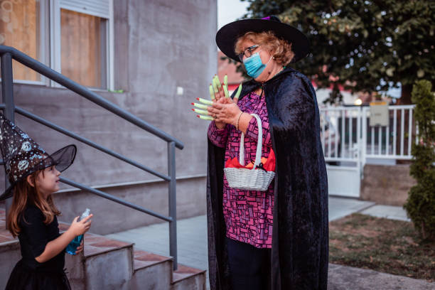 starsza kobieta trzymająca się za ręce ze swoją wnuczką, obie w kostiumach czarownic na halloween - color image halloween people elegance zdjęcia i obrazy z banku zdjęć