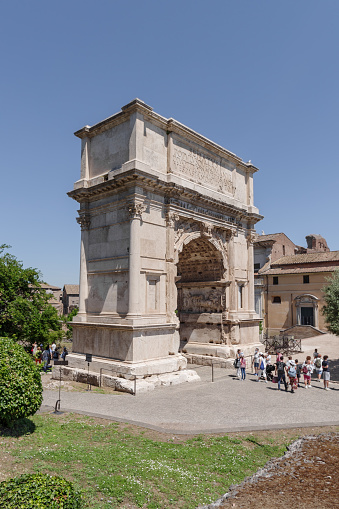 Rome, Italy - June 12, 2021: The Arch of Titus, a triumphal arch built by the Emperor Domitian around 81 A.D. on the Sacra street, the main road in the Roman Forum in Rome. People exploring the surrounding area