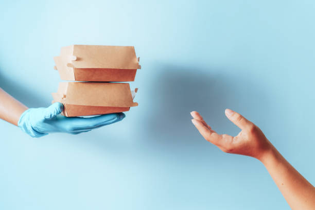 Hand in blue glove passes paper food containers to the other hand against blue background stock photo