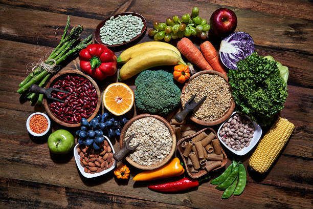 Top view of dietary fiber fresh vegan food and legumes on rustic wooden table. Healthy food themes with frame and copy space. Dietary and healthy food themes. Table top view of fresh vegetables and legumes on rustic wooden table. Food is rich of fiber ideal for dieting and healthy eating. Includes corn, avocado, broccoli, orange fruit, grapes, bell pepper, lettuce, banana, apple  almonds and wholegrain pasta. dietary fiber photos stock pictures, royalty-free photos & images