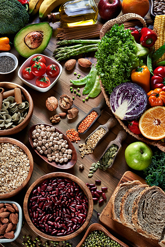 Dietary and healthy food themes. High angle view of fresh vegetables and legumes on rustic wooden table. Food is rich of fiber ideal for dieting and healthy eating. Includes corn, avocado, broccoli, orange fruit, grapes, bell pepper, lettuce, banana, apple  almonds and wholegrain pasta, bread.