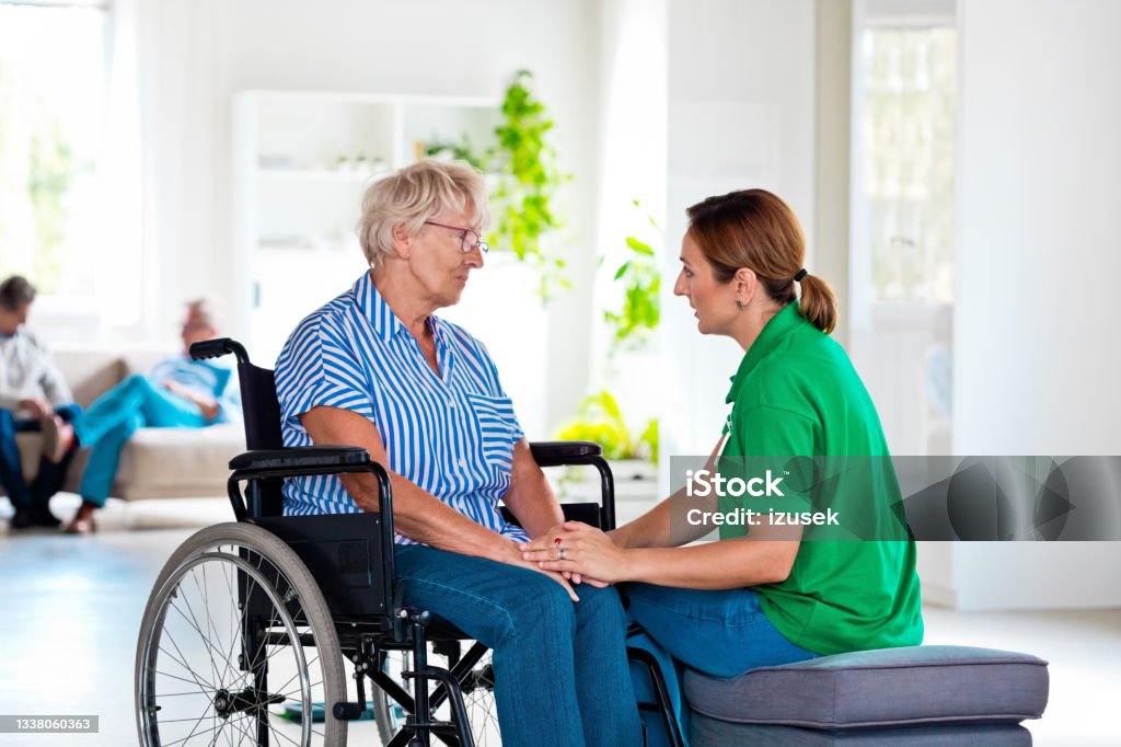 Home nurese consoling senior woman Worried elderly lady sitting in wheelchair in retirement house. Female social worker consoling senior woman. Nurse Stock Photo