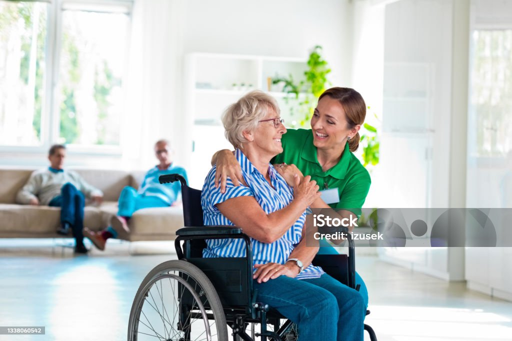 Senior woman talking with nurse in retirement house Friendly female social worker talking with senior woman in retirement house. Elderly lady sitting in wheelchair. Nurse Stock Photo