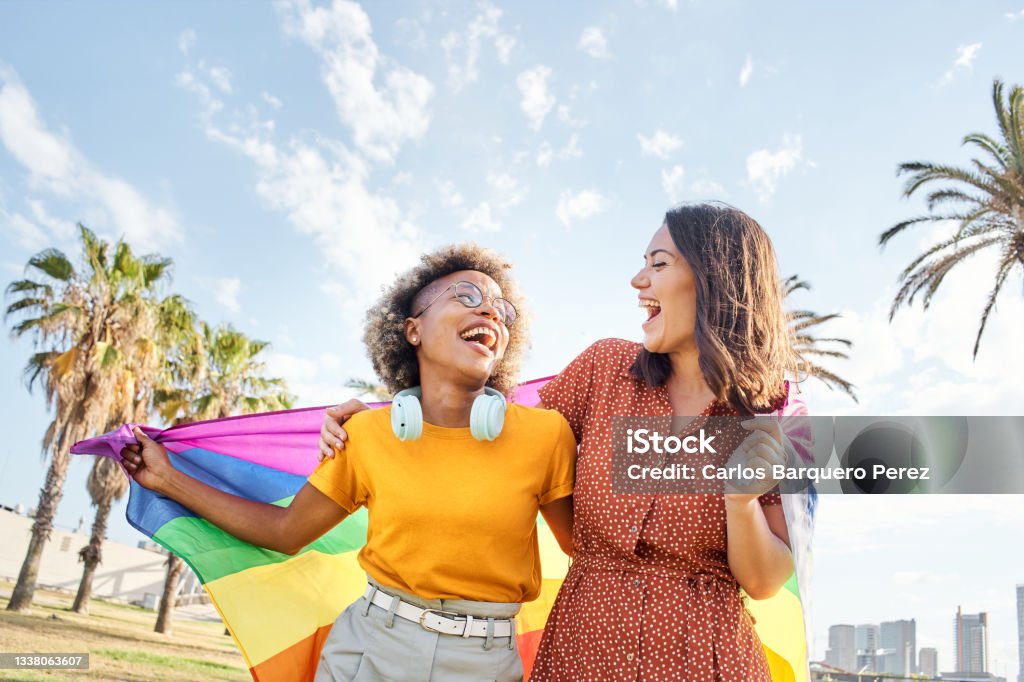 Lesbian loving couple looking at each other with rainbow flag. Concept of pride, homosexual, equality, freedom. LGBTQIA Rights Stock Photo