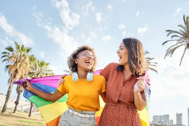 Lesbian loving couple looking at each other with rainbow flag. Concept of pride, homosexual, equality, freedom.