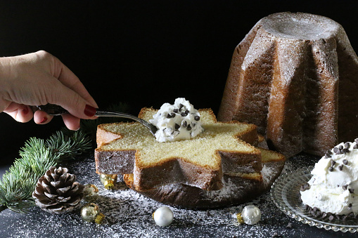 Slice of Pandoro traditional Italian Christmas cake with cream and chocolate granules on dark background.