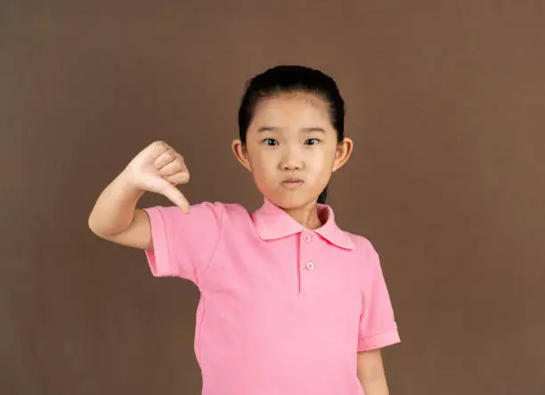 Photo of Little Girl Thumbs Down on Brown Background