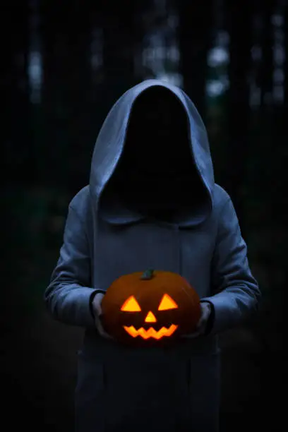Mysterious figure in monk or wizard costume holding carved Jack-o-lantern pumpkin head. Halloween concept.