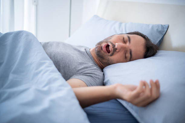 un hombre que se queda dormido y ronca en la cama - apnea del sueño fotografías e imágenes de stock