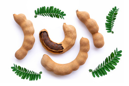 Tamarind (Tamarindus) fruit with green leaves isolated on white backgrund. Top view. Flat lay.