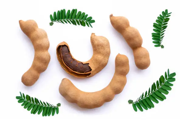 Tamarind (Tamarindus) fruit with green leaves isolated on white backgrund. Top view. Flat lay.